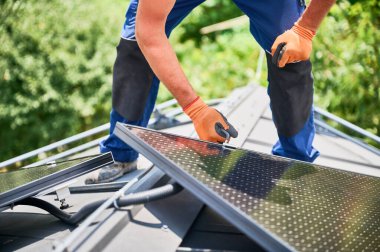 Evin çatısında fotovoltaik güneş paneli inşa eden bir işçi. Güneş modülünü takan eldivenlerdeki adam mühendis hex anahtarı yardımıyla dışarı çıkıyor. Alternatif ve yenilenebilir enerji üretimi kavramı.