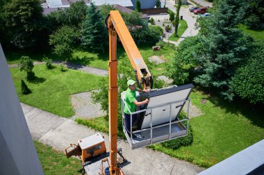 İşçiler vinç kaldırarak evin metal çatısındaki fotovoltaik güneş panelini kaldırıyorlar. Dışarıya fotovoltaik güneş modülleri kuran adamlar. Yenilenebilir enerji üretimi kavramı.
