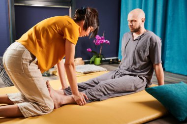 Masör Tayland yogası masajı yapıyor. Kadın terapist erkek hasta için evde geleneksel masaj tedavisi uyguluyor. Kel müşteri paspasın üzerinde uzanıyor, meditasyon yapıyor, sakin atmosferde el masajının keyfini çıkarıyor..