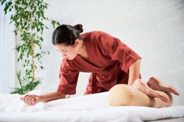 Masseuse making thai yoga massage. Woman therapist doing traditional massage treatment for female patient using elbow. Client lying on mat, meditating, enjoying hand massage in calm atmosphere.