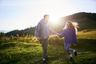 Erkek ve kadın el ele tutuşup güneşli çayırlarda yürüyorlar. Güneş arkada batıyor, sahne üzerine sıcak bir parıltı saçıyor. Gülüşleri ve akan manzaraları mutluluk ve bağlantı anlarını yakalıyor..