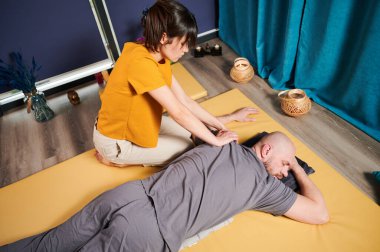 Masör Tayland yogası masajı yapıyor. Kadın terapist erkek hasta için evde geleneksel masaj tedavisi uyguluyor. Kel müşteri paspasın üzerinde uzanıyor, meditasyon yapıyor, sakin atmosferde el masajının keyfini çıkarıyor..