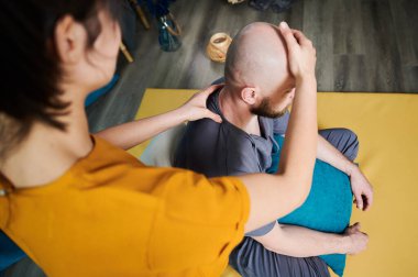 Masör Tayland yogası masajı yapıyor. Kadın terapist erkek hasta için evde geleneksel masaj tedavisi uyguluyor. Kel müşteri paspasın üzerinde oturuyor, meditasyon yapıyor, sakin bir atmosferde el masajının keyfini çıkarıyor..