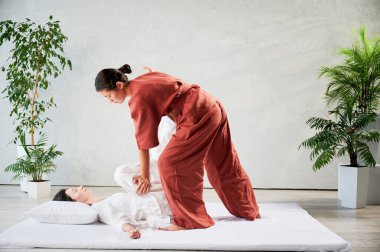 Masör Tayland yogası masajı yapıyor. Geleneksel masaj tedavisi uygulayan kadın terapist, kadın hastaların vücudunu geriyor. Müşteri paspasın üzerinde uzanıyor, sakin atmosferde el masajının keyfini çıkarıyor..