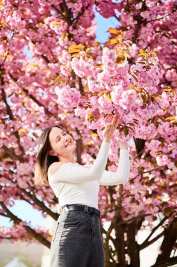 Alerjisi olan bir kadın, bahardaki sezonluk alerjiden zevk alıyor. Baharda çiçek açan sakura ağacının önünde gülümseyen güzel bir kadının portresi. Bahar alerjisi konsepti.