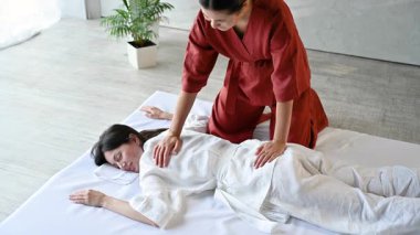 Masör Tayland yogası masajı yapıyor. Kadın terapist, kadın hasta için evde geleneksel masaj tedavisi uyguluyor. Müşteri paspasın üzerinde uzanıyor, meditasyon yapıyor, sakin bir atmosferde el masajının keyfini çıkarıyor..