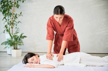 Masör Tayland yogası masajı yapıyor. Kadın terapist, kadın hasta için evde geleneksel masaj tedavisi uyguluyor. Müşteri paspasın üzerinde uzanıyor, meditasyon yapıyor, sakin bir atmosferde el masajının keyfini çıkarıyor..