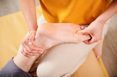 Masör Tayland yogası masajı yapıyor. Kadın terapist, erkek hastaların ayaklarına geleneksel masaj yapıyor. Kapatın. Müşteri paspasın üzerinde uzanıyor, meditasyon yapıyor, sakin bir atmosferde el masajının keyfini çıkarıyor..