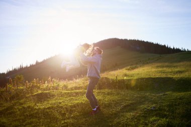 Baba sevinçle kızını havaya kaldırır, hem güler hem de batan güneşin altın parıltısıyla yıkanır. Çimenli çayırlarda, tepeler ve orman zeminleri olan bir adam ve çocuk..