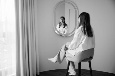 Güzel kız aynada kendine bakıyor ve gülümsüyor. Kendini kontrol eden güzel bir kadın. Evdeki aynanın karşısında oturan sevimli kız. Siyah ve beyaz resim.