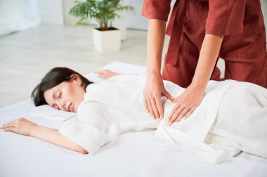 Masör Tayland yogası masajı yapıyor. Kadın hastaya geleneksel masaj yapan kadın terapist görüşü. Müşteri paspasın üzerinde uzanıyor, meditasyon yapıyor, sakin bir atmosferde el masajının keyfini çıkarıyor..