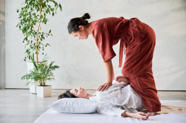 Masör Tayland yogası masajı yapıyor. Geleneksel masaj tedavisi uygulayan kadın terapist, kadın hastaların vücudunu geriyor. Müşteri paspasın üzerinde uzanıyor, sakin atmosferde el masajının keyfini çıkarıyor..