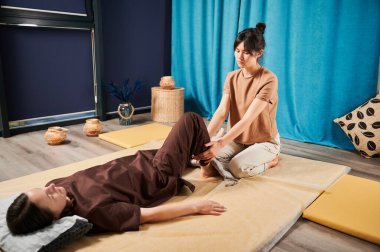 Masör Tayland yogası masajı yapıyor. Kadın terapist, kadın hasta için evde geleneksel masaj tedavisi uyguluyor. Müşteri paspasın üzerinde uzanıyor, meditasyon yapıyor, sakin bir atmosferde el masajının keyfini çıkarıyor..