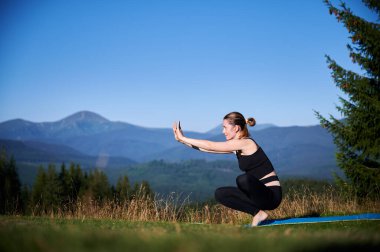 Dağlarda yoga yapan bir kadın, sakin, doğal bir ortamda. Kadın yoga pozu veriyor paspasın üzerinde, gün doğumunda ya da günbatımında güzel dağ manzarasının arka planıyla.