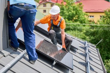 İşçiler evin çatısına güneş paneli inşa ediyorlar. Dışarıda fotovoltaik güneş modülü kuran kask takan iki adam. Alternatif, yeşil ve yenilenebilir enerji üretimi kavramı.