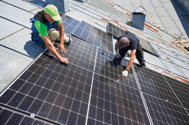 İşçiler evin metal çatısında güneş paneli inşa ediyorlar. İki adam dışarı fotovoltaik güneş modülü kuruyor. Alternatif, yeşil ve yenilenebilir enerji üretimi kavramı.