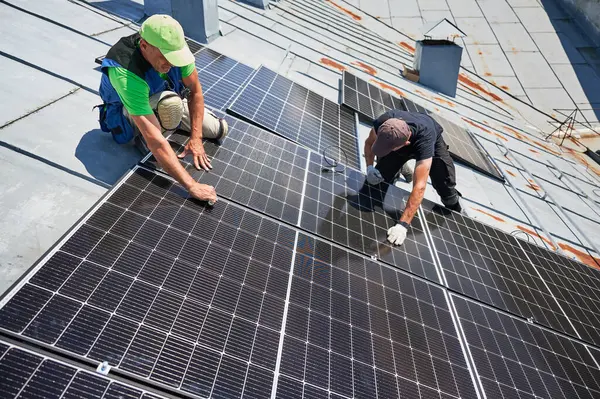 İşçiler evin metal çatısında güneş paneli inşa ediyorlar. İki adam dışarı fotovoltaik güneş modülü kuruyor. Alternatif, yeşil ve yenilenebilir enerji üretimi kavramı.