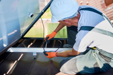 İşçi evin çatısına güneş panelleri kuruyor. Elektrikçinin kabloları özel bir kravatla güvence altına aldığına dair yakın görüş. Alternatif ve yenilenebilir enerji kavramı.