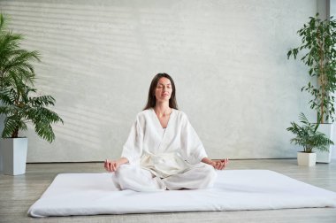 Beyaz elbiseli güzel kadın Tayland masajından önce nilüfer pozisyonunda oturmuş yoga yapıyor..