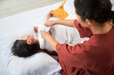 Masör Tayland yogası masajı yapıyor. Kadın hasta için geleneksel masaj tedavisi uygulayan kadın terapist. Müşteri paspasın üzerinde uzanıyor, meditasyon yapıyor, sakin bir atmosferde el masajının keyfini çıkarıyor. Kırpılmış görünüm.