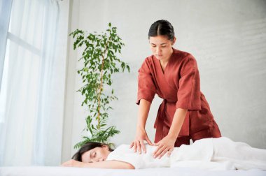 Masör Tayland yogası masajı yapıyor. Kadın terapist, kadın hasta için evde geleneksel masaj tedavisi uyguluyor. Müşteri paspasın üzerinde uzanıyor, meditasyon yapıyor, sakin bir atmosferde el masajının keyfini çıkarıyor..