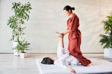 Masör Tayland yogası masajı yapıyor. Geleneksel masaj tedavisi uygulayan kadın terapist, kadın hastaların vücudunu geriyor. Müşteri paspasın üzerinde uzanıyor, sakin atmosferde el masajının keyfini çıkarıyor..