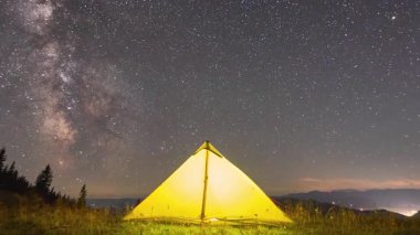 Zaman aşımı. Yıldızlarla ve Samanyolu 'yla dolu büyüleyici gece göğünün altında parlayan sarı çadır. Çimenli tarlalar ve gölgeli çam ağaçlarıyla çevrili. Doğada kamp yapmanın güzelliği ve sükuneti..