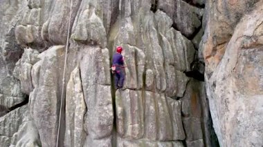 Erkek kaya tırmanıcısının engebeli kireçtaşı kayalıklara tırmanırken güvenlik için koşum takımı ve ip ile hava görüntüsü. Sporcu Ukrayna 'nın Karpatya dağlarındaki Dobvush Kayaları' nda dikey büyük kaya parçasına tırmanıyor.