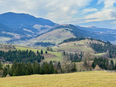 Yoğun ormanlara ve parçalı bulutlu gökyüzünün altındaki uzak dağlara uzanan verimli yeşil tarlalar. Dağınık evler ve çiftlikler vadiyi dolduruyor..