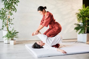 Masör Tayland yogası masajı yapıyor. Geleneksel masaj tedavisi uygulayan kadın terapist, kadın hastaların vücudunu geriyor. Müşteri paspasın üzerinde uzanıyor, sakin atmosferde el masajının keyfini çıkarıyor..