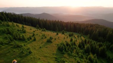Otlak yamaçtaki hava manzaralı çadırlar yemyeşil ve küçük ağaçların arasına dağılmış durumda. Güneşin altın rengi. Uzakta, yuvarlanan dağların katmanları ufukta kaybolur..