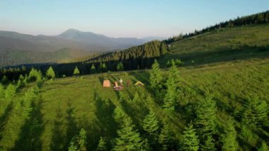 Otlak yamaçtaki hava manzaralı çadırlar yemyeşil ve küçük ağaçların arasına dağılmış durumda. Güneşin altın rengi. Uzakta, yuvarlanan dağların katmanları ufukta kaybolur..