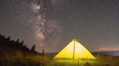 Zaman aşımı. Yıldızlarla ve Samanyolu 'yla dolu büyüleyici gece göğünün altında parlayan sarı çadır. Çimenli tarlalar ve gölgeli çam ağaçlarıyla çevrili. Doğada kamp yapmanın güzelliği ve sükuneti..