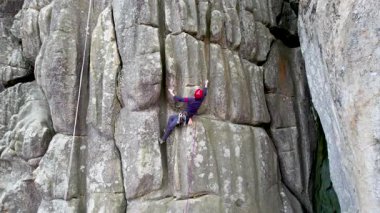 Erkek kaya tırmanıcısının engebeli kireçtaşı kayalıklara tırmanırken güvenlik için koşum takımı ve ip ile hava görüntüsü. Sporcu Ukrayna 'nın Karpatya dağlarındaki Dobvush Kayaları' nda dikey büyük kaya parçasına tırmanıyor.