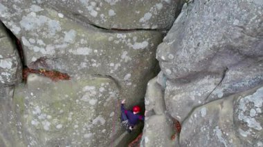 Erkek kaya tırmanıcısının engebeli kireçtaşı kayalıklara tırmanırken güvenlik için koşum takımı ve ip ile hava görüntüsü. Sporcu Ukrayna 'nın Karpatya dağlarındaki Dobvush Kayaları' nda dikey büyük kaya parçasına tırmanıyor.