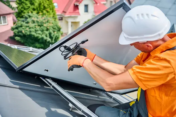 Evin metal çatısında güneş paneli inşa eden bir işçi. Erkek teknisyen dışarıda fotovoltaik güneş modülü kurmaya hazırlanıyor. Alternatif, yeşil ve yenilenebilir enerji üretimi kavramı.