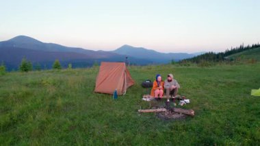 Sabah kampının havadan görünüşü. Gün batımında kamp alanı. Çadırları hep yeşil ağaçların arasında. Kampçılar yakınlarda oturuyor, dalgalı günbatımına doğru yuvarlanan tepelerin üzerinde. Karpatya dağlarında resim gibi bir manzara.