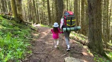 Anne ve küçük kızı güneş ışığıyla aydınlanan ormanda el ele yürüyorlar. Kadın kamp malzemeleriyle birlikte büyük bir sırt çantası taşırken, çocuk hevesle onu takip ediyor. Uzun ağaçlar ve yemyeşil patikalar..