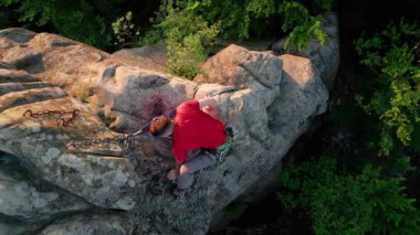 Erkek kaya tırmanıcısının engebeli kireçtaşı kayalıklara tırmanırken güvenlik için koşum takımı ve ip ile hava görüntüsü. Sporcu Ukrayna 'nın Karpatya dağlarındaki Dobvush Kayaları' nda dikey büyük kaya parçasına tırmanıyor.
