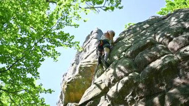 Erkek kaya tırmanışçısı güvenlik için kayış takımı ve iple engebeli kireçtaşı uçurumuna tırmanıyor. Sporcu Ukrayna 'nın Karpatya dağlarındaki Dobvush Kayaları' nda dikey büyük kaya parçasına tırmanıyor.