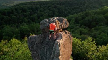 Erkek kaya tırmanıcısının engebeli kireçtaşı kayalıklara tırmanırken güvenlik için koşum takımı ve ip ile hava görüntüsü. Sporcu Ukrayna 'nın Karpatya dağlarındaki Dobvush Kayaları' nda dikey büyük kaya parçasına tırmanıyor.
