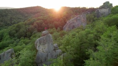 Ukrayna 'daki Karpat Dağları' ndaki Dovbush Kayalıkları 'ndaki kaya oluşumunun havada görünen görüntüsü. Güneş batıyor, yemyeşil orman, uzak tepeler üzerine ılık bir parıltı saçıyor, nefes kesici bir manzara yaratıyor..