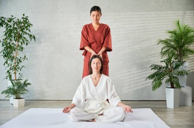 Masör Tayland yogası masajı yapıyor. Kadın terapist, kadın hasta için evde geleneksel masaj tedavisi uyguluyor. Müşteri mindere oturuyor, meditasyon yapıyor, sakin bir atmosferde el masajının keyfini çıkarıyor..