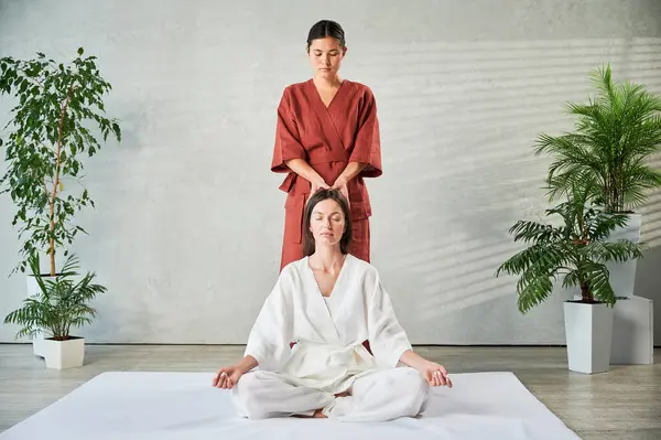 Masör Tayland yogası masajı yapıyor. Kadın terapist, kadın hasta için evde geleneksel masaj tedavisi uyguluyor. Müşteri mindere oturuyor, meditasyon yapıyor, sakin bir atmosferde el masajının keyfini çıkarıyor..