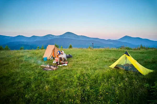 Sabahları iki çadırı olan manzaralı dağ kampı. İki kampçı, bulutsuz gökyüzünün altında yuvarlanan dağların huzurlu manzarasının keyfini çıkarıyorlar. Resimli gündoğumu manzarası, huzurlu ve rahat bir açık hava deneyimi yaratıyor..