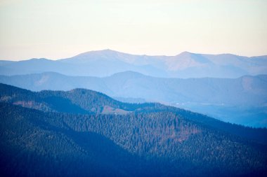 Mavi ve yeşilin gölgelerinde yuvarlanan dağların sakin manzarası, yumuşak, pastel gökyüzünün altında uzak tepeler, huzurlu ve huzurlu bir manzara yaratıyor..