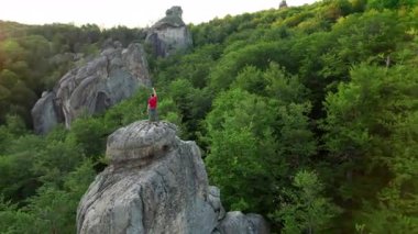 Ukrayna 'daki Karpat Dağları' ndaki Dovbush Kayalıkları 'ndaki kaya oluşumunun havada görünen görüntüsü. Güneş batıyor, yemyeşil orman, uzak tepeler üzerine ılık bir parıltı saçıyor, nefes kesici bir manzara yaratıyor..