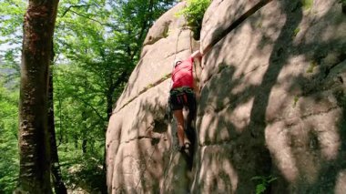 Erkek kaya tırmanıcısının engebeli kireçtaşı kayalıklara tırmanırken güvenlik için koşum takımı ve ip ile hava görüntüsü. Sporcu Ukrayna 'nın Karpatya dağlarındaki Dobvush Kayaları' nda dikey büyük kaya parçasına tırmanıyor.