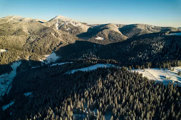 Karla kaplı tarlalar ve yoğun çam ormanlarıyla nefes kesici kış manzarası. Ağaçların arasına kurulmuş küçük bir köy. Uzak dağlar görkemli bir şekilde masmavi gökyüzünün altında duruyor..