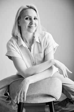 Bar taburesinde rahatlayan güzel bir kadın. Kameraya gülümseyen sarı saçlı kadın portresi. Evinde bar taburesinde oturan güzel bir kadın. Siyah ve beyaz resim.